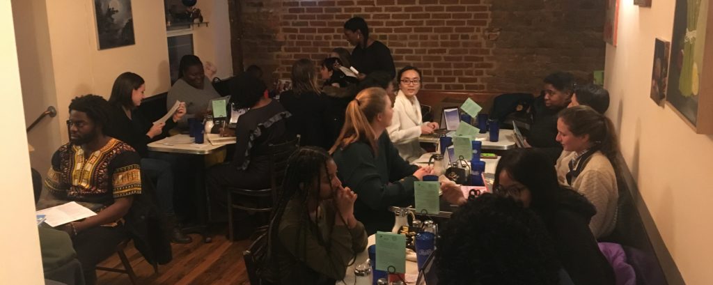 People sitting at tables. The people are a variety of races and ages. Most are women. They are all engaged in small group conversations.